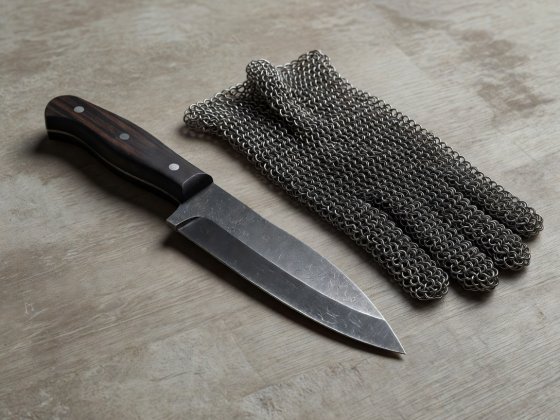 Soft-lit 3D illustration of a forged steel oyster shucking knife beside a chainmail protective glove